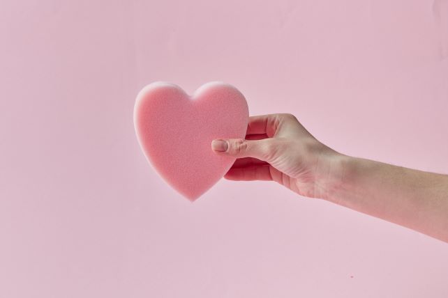 En hand håller fram ett stort rosa hjärta. 